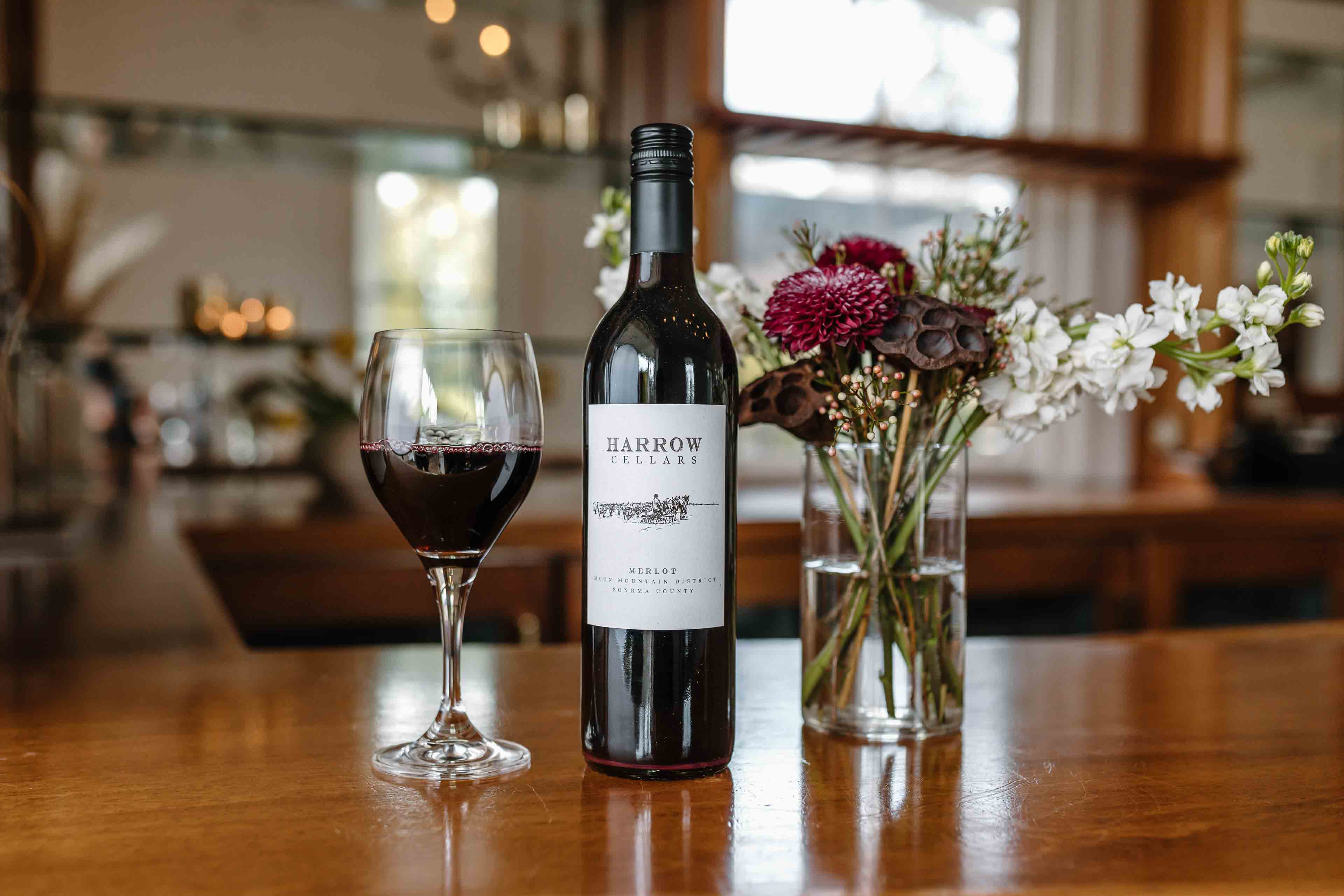 A Bottle of Harrow Cellars Red Wine On A Bar With Flowers